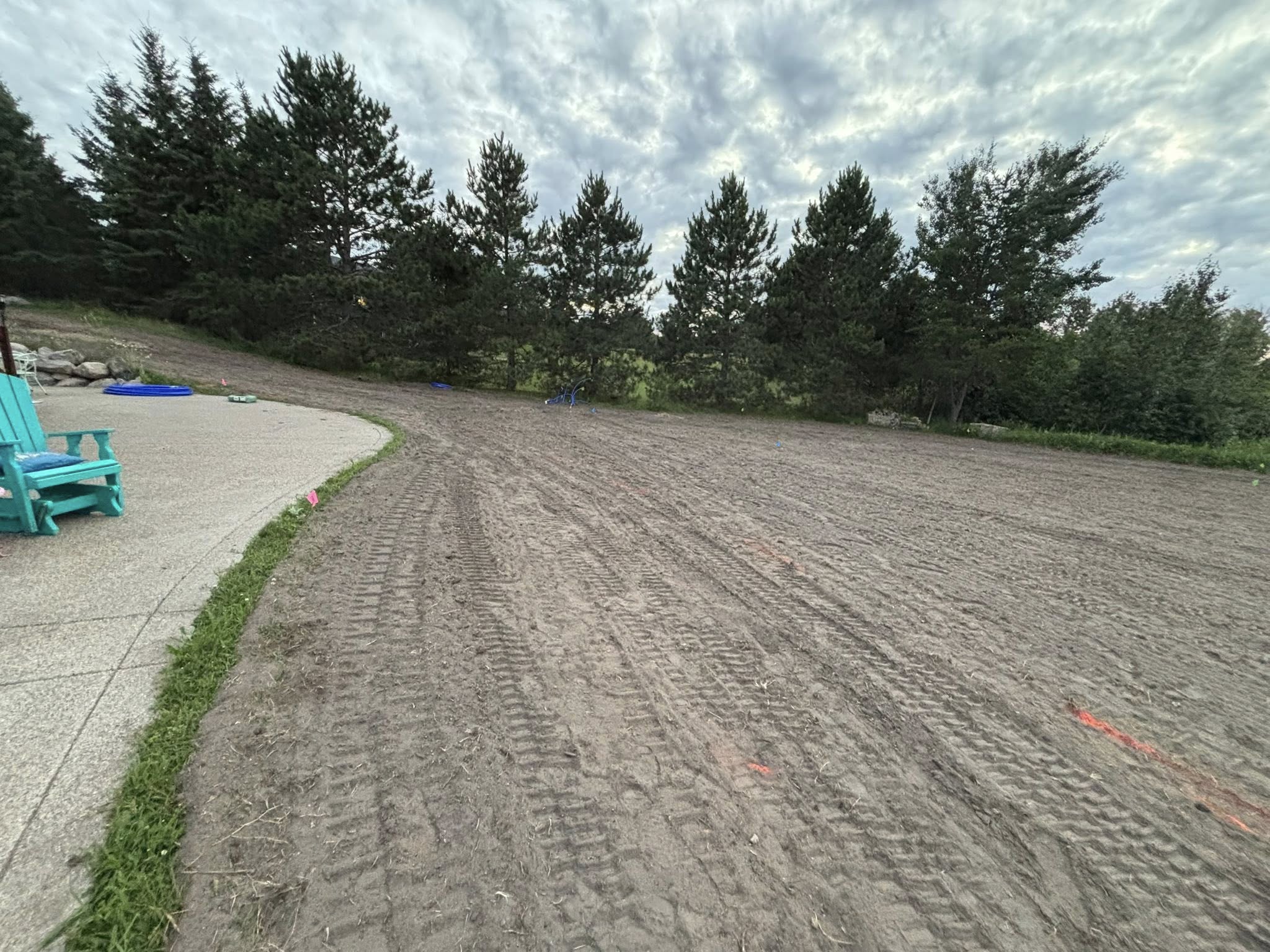 Skid steer track marks on freshly graded dirt next to concrete patio